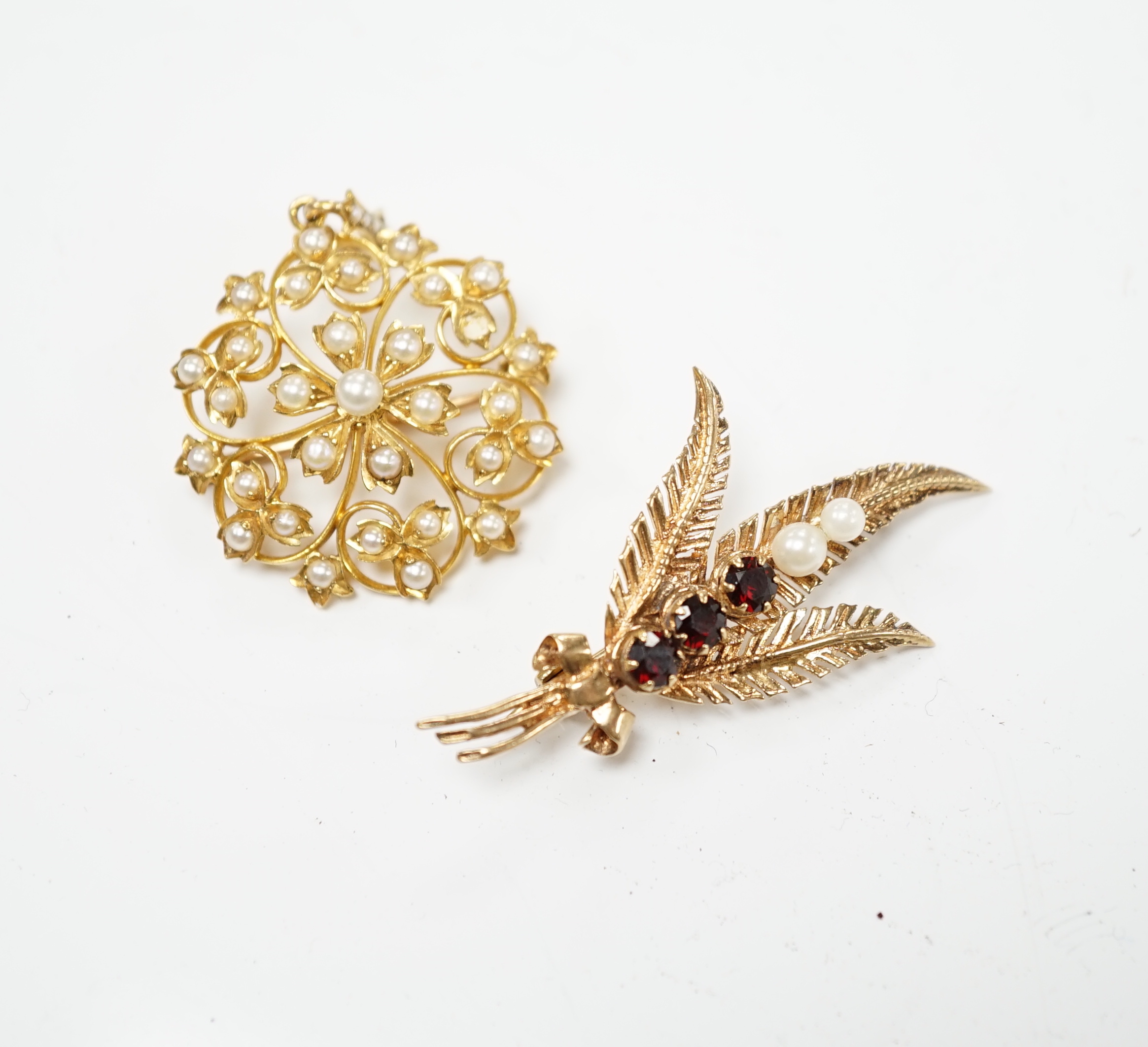 An Edwardian yellow metal and seed pearl set circular cluster pendant brooch, 27mm, gross weight 6.2 grams, together with a later 9ct gold, garnet and cultured pearl set foliate brooch, gross weight 4.1 grams.